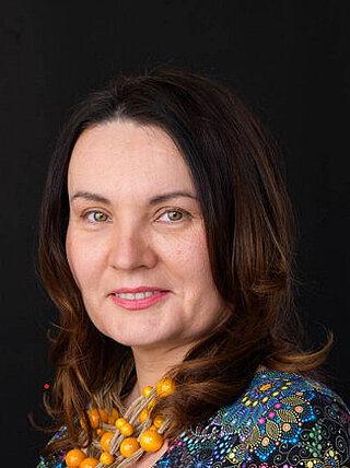 Kobieta w średnim wieku z ciemnymi długimi włosami i kolorowej bluzce.